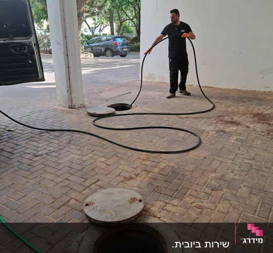 אדם מחזיק צינור ליד פתח ביוב פתוח